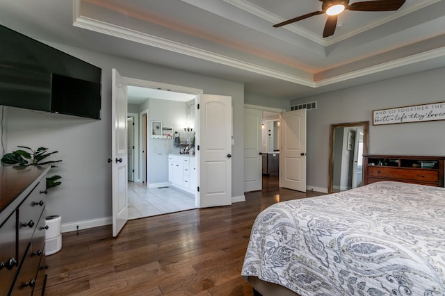 bedroom featuring a raised ceiling, crown molding, wood finished floors, baseboards, and ensuite bath