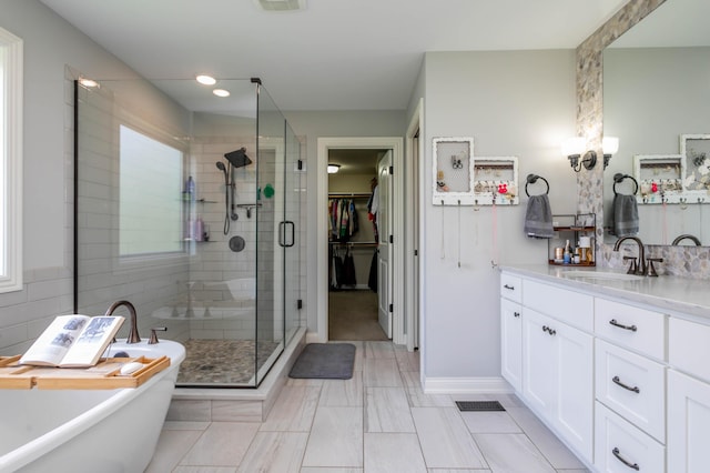 full bath featuring a stall shower, vanity, a freestanding tub, a spacious closet, and baseboards