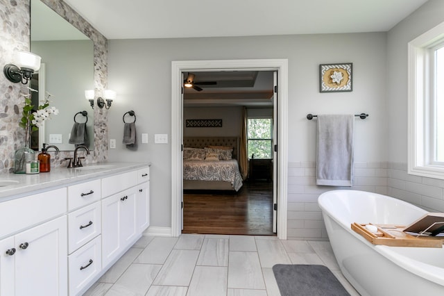 bathroom with healthy amount of natural light, ensuite bathroom, double vanity, a freestanding tub, and tile walls