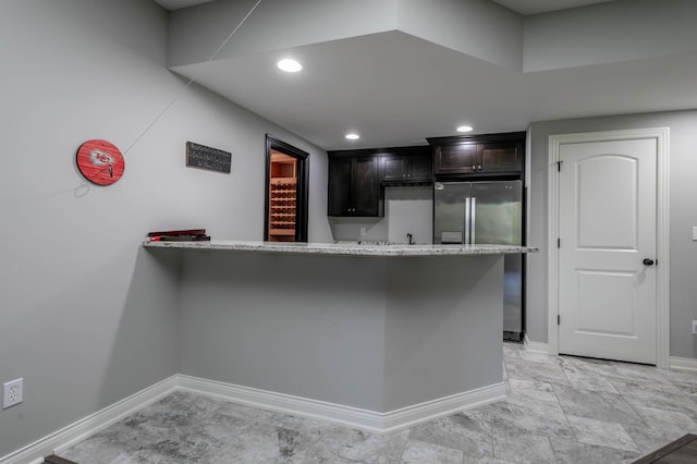 kitchen featuring stainless steel fridge, baseboards, a peninsula, dark brown cabinets, and light stone counters