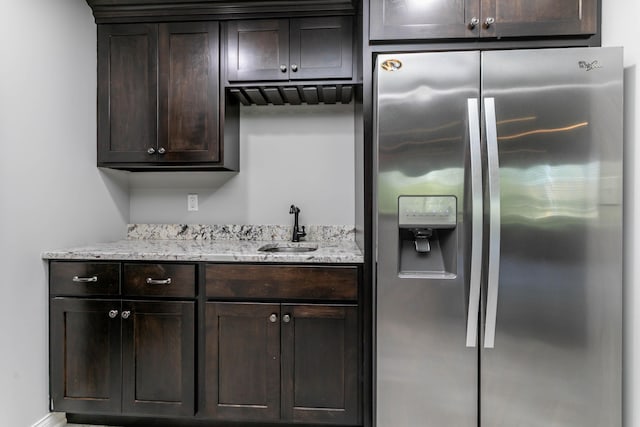 kitchen with stainless steel fridge with ice dispenser, a sink, dark brown cabinets, and light stone counters