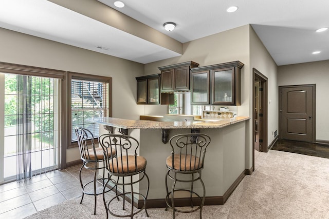 4710 Winding Wood Ct, Columbia, MO 65203 - kitchen with dark brown cabinets, light stone countertops, a breakfast bar area, a peninsula, and recessed lighting