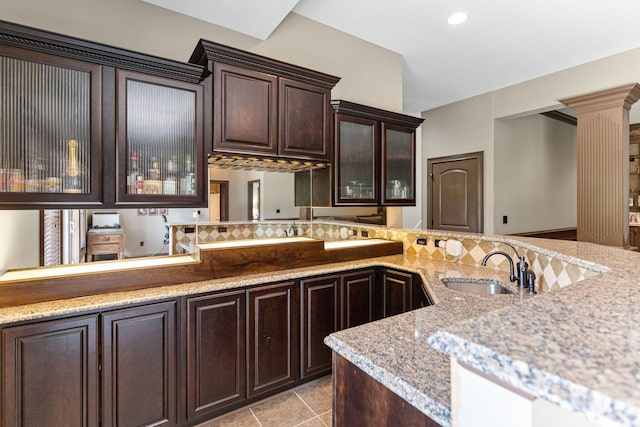 4710 Winding Wood Ct, Columbia, MO 65203 - kitchen with decorative columns, dark brown cabinets, glass insert cabinets, light tile patterned floors, and light stone counters
