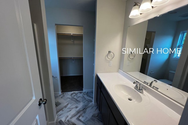 bathroom featuring vanity, toilet, a spacious closet, baseboards, and marble look tile flooring