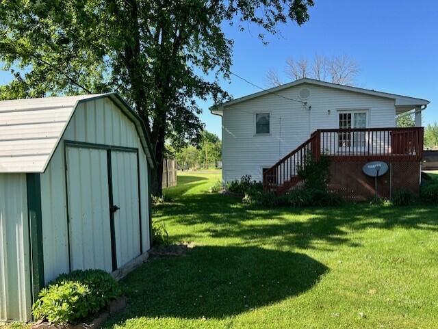 view of green lawn with a storage unit, an outbuilding, and a deck