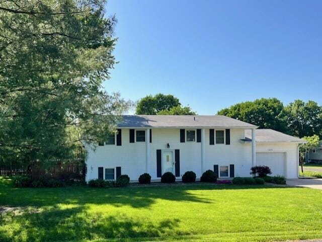raised ranch featuring an attached garage, a front lawn, and driveway
