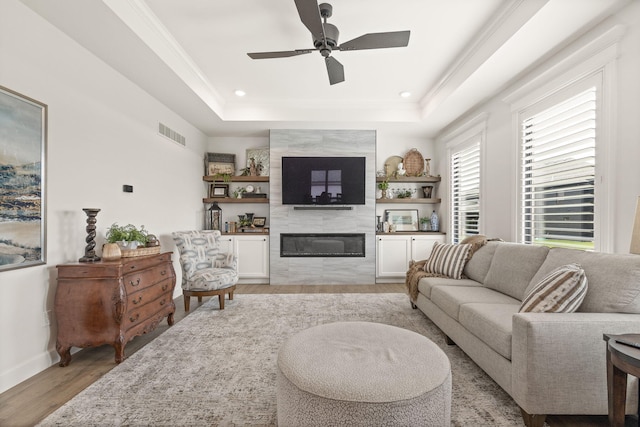 1104 Caymus Ct, Columbia, MO 65201 - living room featuring a tile fireplace, light wood-type flooring, a tray ceiling, a ceiling fan, and crown molding