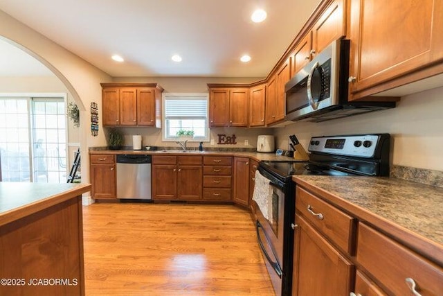1200 Choctaw Ridge Dr, Holts Summit, MO 65043 - kitchen featuring appliances with stainless steel finishes, a sink, brown cabinetry, arched walkways, and light wood finished floors