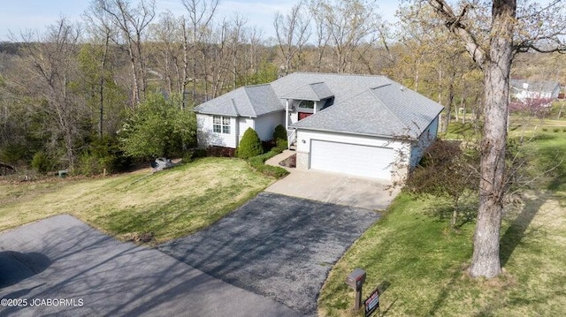 view of front of house with a front yard, driveway, an attached garage, and a view of trees