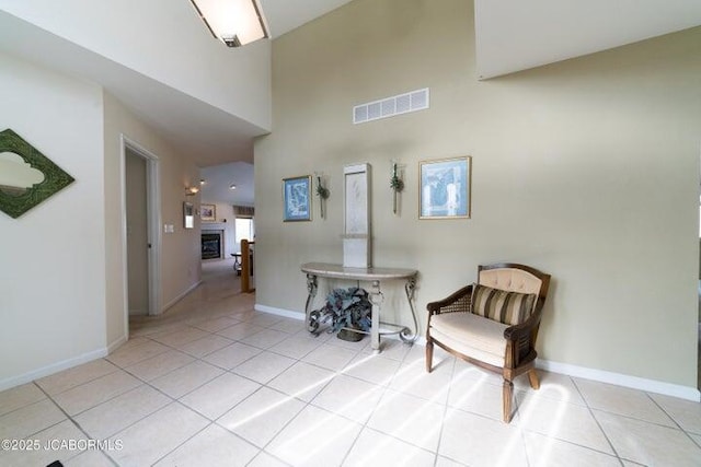 sitting room with a towering ceiling, light tile patterned floors, baseboards, and a glass covered fireplace