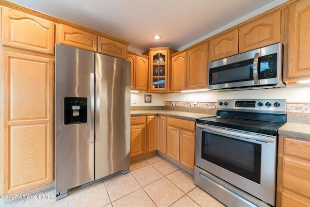 kitchen with appliances with stainless steel finishes, glass insert cabinets, light tile patterned floors, and recessed lighting