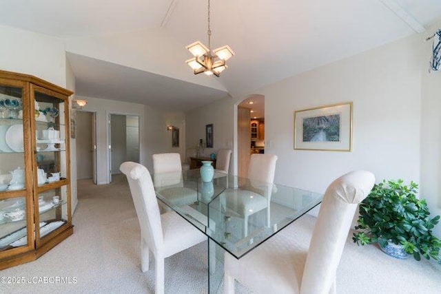 dining room featuring lofted ceiling, light carpet, a chandelier, and arched walkways