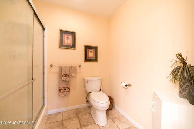 bathroom with toilet, an enclosed shower, tile patterned flooring, and baseboards