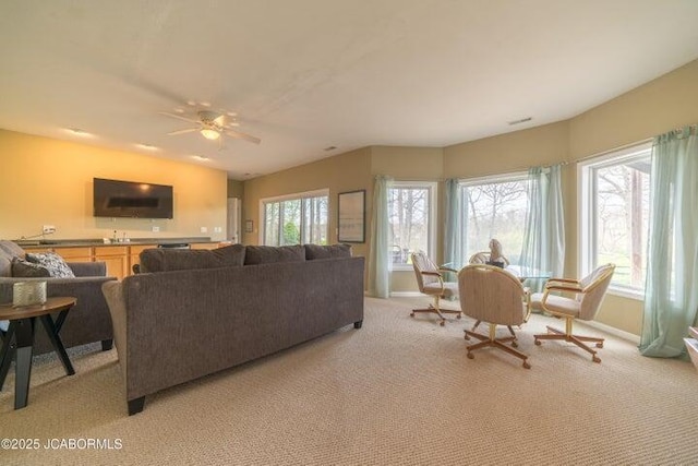living area featuring light colored carpet, baseboards, and a ceiling fan