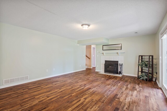 2313 Katy Ln, Columbia, MO 65203 - unfurnished living room with wood finished floors, a tiled fireplace, a textured ceiling, baseboards, and stairs