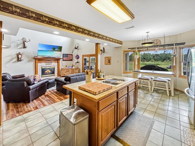 7495 E Schooler Rd, Centralia, MO 65240 - kitchen featuring white electric stovetop, light tile patterned floors, brown cabinets, freestanding refrigerator, and a glass covered fireplace