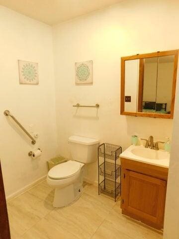 half bath featuring vanity, toilet, tile patterned floors, and baseboards