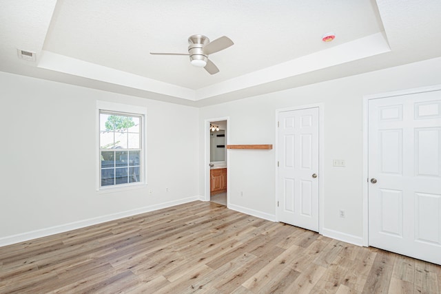 1050 Azoros Dr, Columbia, MO 65203 - unfurnished bedroom featuring a tray ceiling, light wood-type flooring, baseboards, connected bathroom, and ceiling fan