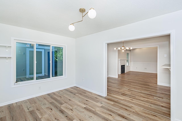 1050 Azoros Dr, Columbia, MO 65203 - unfurnished room featuring a chandelier, light wood-style floors, a fireplace, and a textured ceiling