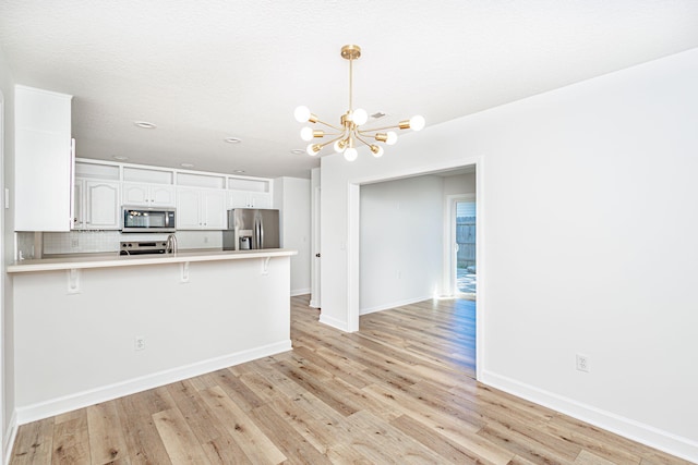 1050 Azoros Dr, Columbia, MO 65203 - kitchen with stainless steel appliances, a chandelier, a peninsula, white cabinets, and a kitchen bar