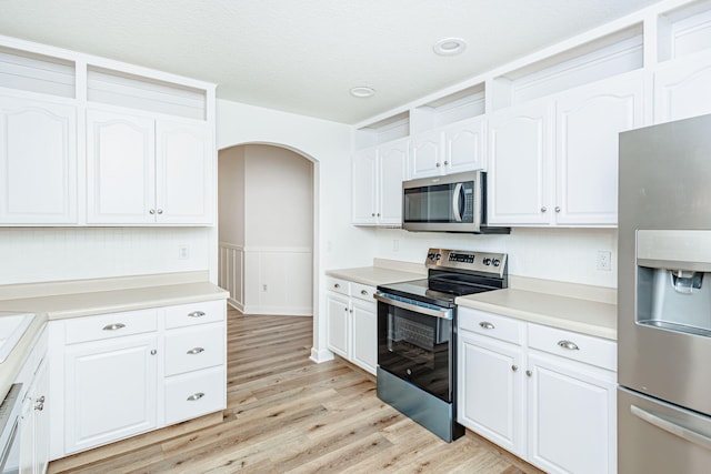 1050 Azoros Dr, Columbia, MO 65203 - kitchen with stainless steel appliances, white cabinetry, light wood-style floors, arched walkways, and wainscoting