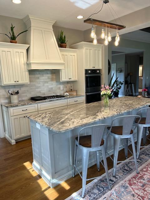 15172 S Henry Ln, Ashland, MO 65010 - kitchen featuring custom range hood, black appliances, a kitchen bar, dark wood-style floors, and light stone countertops