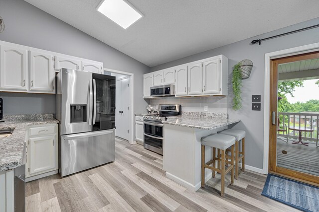 109 N Linnwood Dr, Linn, MO 65051 - kitchen featuring stainless steel appliances, vaulted ceiling, white cabinetry, light wood-type flooring, and light stone countertops