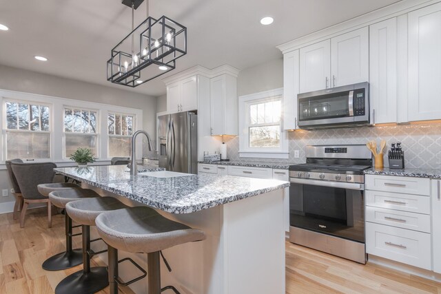 303 S Glenwood Ave, Columbia, MO 65203 - kitchen with appliances with stainless steel finishes, tasteful backsplash, a kitchen island with sink, light stone countertops, and light wood finished floors