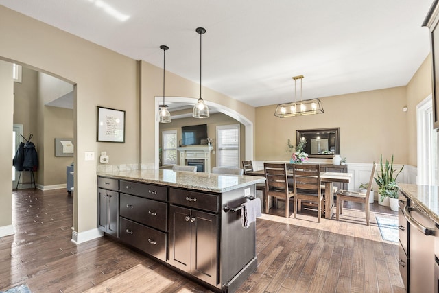 128 Cedar Falls Ct, Columbia, MO 65203 - kitchen with arched walkways, dark wood-style flooring, dark brown cabinetry, a fireplace, and light stone counters