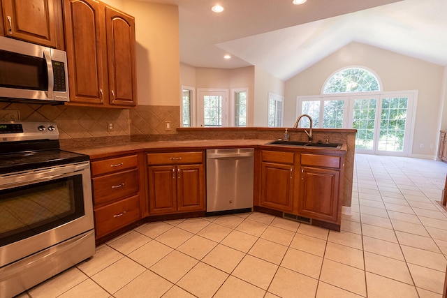 2409 Wild Oak Ct, Columbia, MO 65201 - kitchen featuring stainless steel appliances, vaulted ceiling, a peninsula, light tile patterned flooring, and brown cabinetry