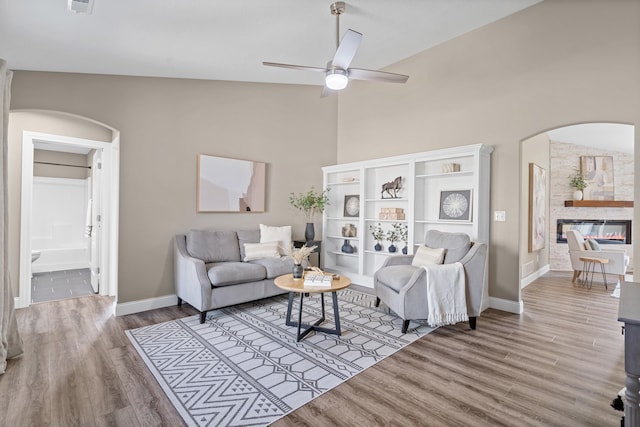 5990 W Tamarack Dr, Columbia, MO 65203 - living room featuring arched walkways, a ceiling fan, wood finished floors, high vaulted ceiling, and a fireplace