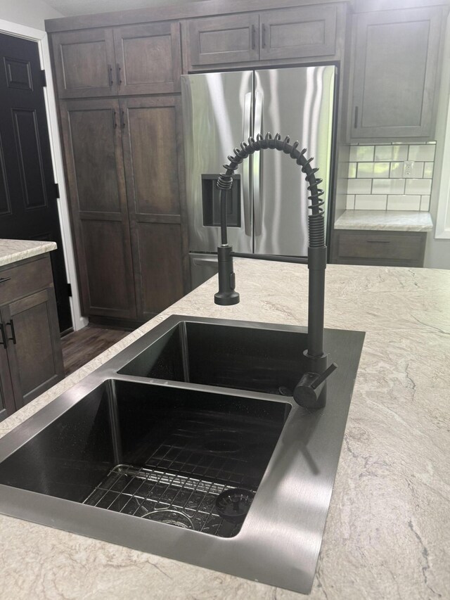 7475 E Lost Woods Ln, Centralia, MO 65240 - kitchen view of stainless steel refrigerator with ice dispenser, a sink, tasteful backsplash, dark brown cabinets, and light stone countertops