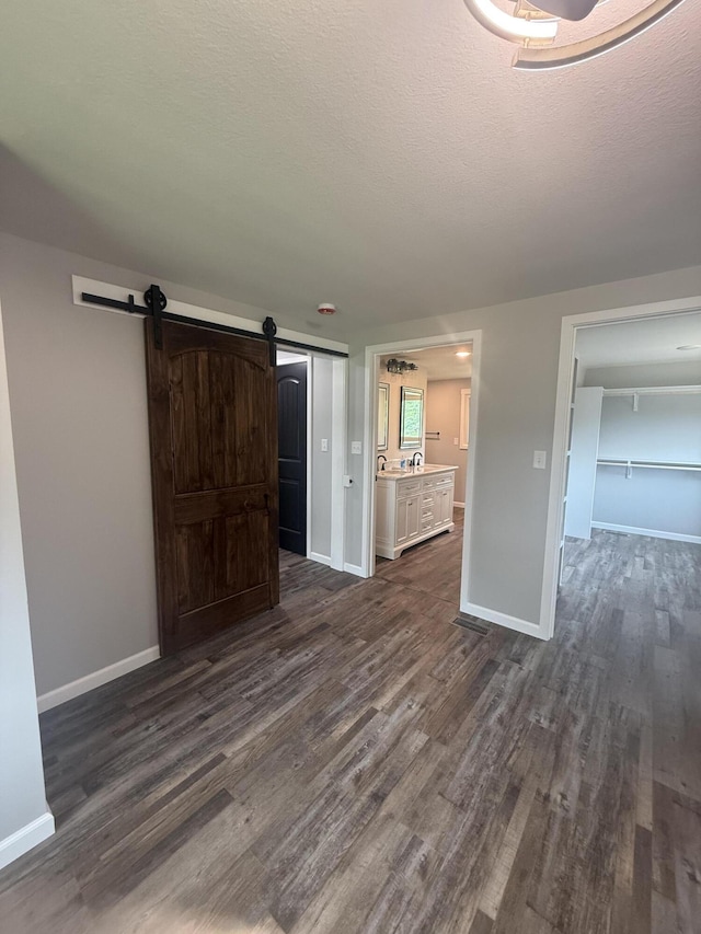 7475 E Lost Woods Ln, Centralia, MO 65240 - unfurnished bedroom with dark wood finished floors, a barn door, baseboards, connected bathroom, and a textured ceiling