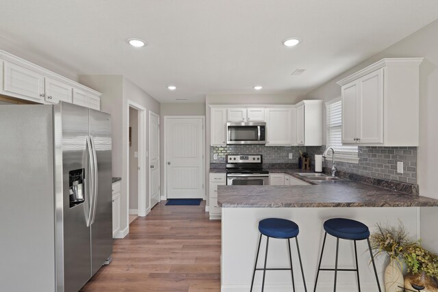5817 Geyser Blvd, Columbia, MO 65202 - kitchen with stainless steel appliances, a sink, a peninsula, light wood-style floors, and decorative backsplash
