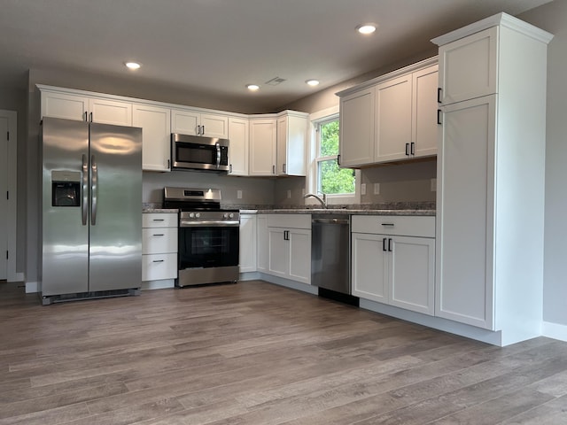 915 Colorado St, Jefferson City, MO 65109 - kitchen featuring appliances with stainless steel finishes, light wood-style floors, dark stone countertops, recessed lighting, and white cabinets