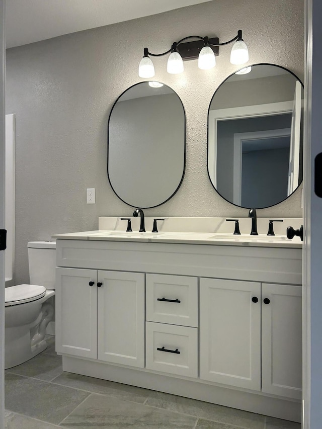 915 Colorado St, Jefferson City, MO 65109 - bathroom with double vanity, toilet, a textured wall, and marble finish floors