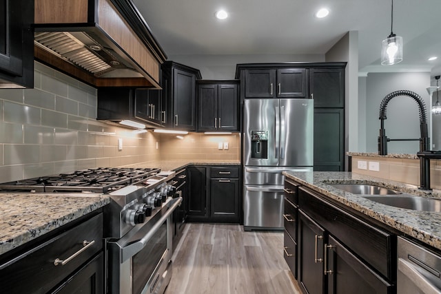 2016 Devonshire Dr, Columbia, MO 65203 - kitchen featuring stainless steel appliances, wall chimney exhaust hood, dark cabinetry, light stone countertops, and hanging light fixtures
