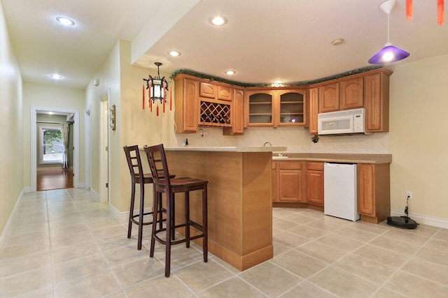 203 Foxwood Ct, Columbia, MO 65203 - kitchen with white microwave, a kitchen bar, light tile patterned floors, recessed lighting, and glass insert cabinets