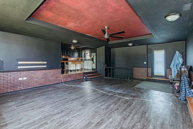 4741 E N Rte E, Columbia, MO 65202 - unfurnished living room with wood finished floors, ceiling fan, a textured ceiling, a tray ceiling, and brick wall