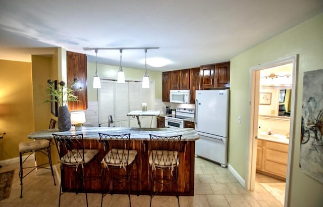 1902 Park Deville Pl, Columbia, MO 65203 - kitchen featuring white appliances, a peninsula, a breakfast bar, decorative light fixtures, and backsplash