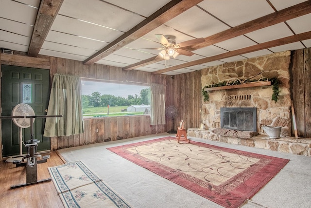 3674 State Road Aa, Holts Summit, MO 65043 - unfurnished living room with beam ceiling, wood walls, a ceiling fan, a stone fireplace, and wood finished floors