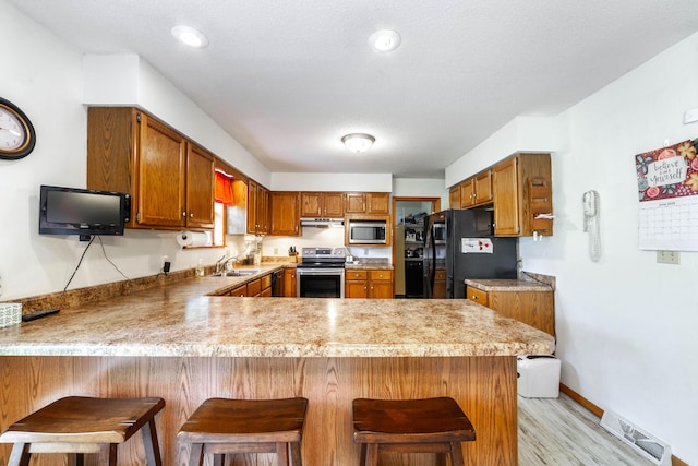 6002 E Molly Ln, Columbia, MO 65202 - kitchen with stainless steel appliances, a peninsula, brown cabinetry, light wood-type flooring, and light countertops