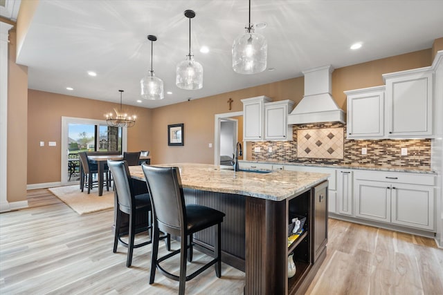 6406 Crooked Switch Ct, Columbia, MO 65201 - kitchen featuring custom exhaust hood, light wood-style floors, decorative backsplash, an island with sink, and light stone countertops