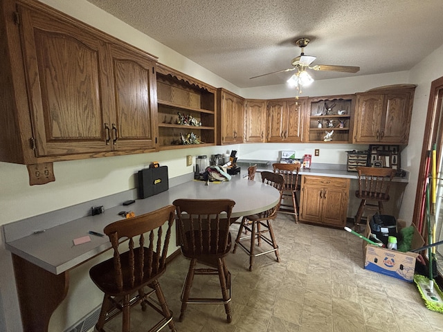 14200 N Yy, Columbia, MO 65202 - kitchen with open shelves, built in desk, brown cabinetry, a ceiling fan, and a textured ceiling