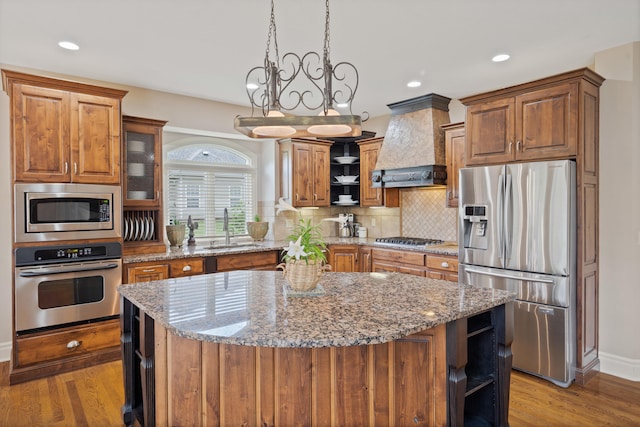 4902 Cochero Ct, Columbia, MO 65203 - kitchen with stainless steel appliances, custom exhaust hood, brown cabinets, light stone counters, and a center island