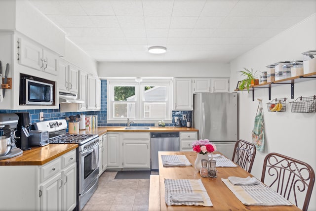 708 Clayton St, Columbia, MO 65203 - kitchen featuring wood counters, appliances with stainless steel finishes, under cabinet range hood, tasteful backsplash, and white cabinets
