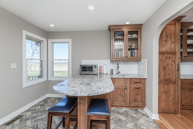 8900 W Graham Rd, Rocheport, MO 65279 - kitchen featuring tasteful backsplash, a kitchen bar, brown cabinets, arched walkways, and glass insert cabinets