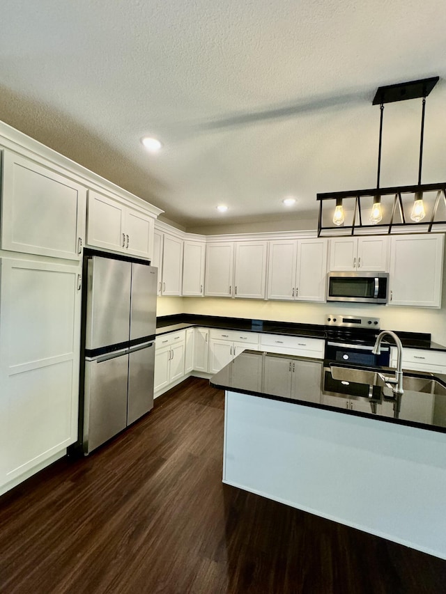 1680 W Fenton Rd, Columbia, MO 65202 - kitchen with stainless steel appliances, dark wood-style flooring, dark countertops, white cabinetry, and hanging light fixtures
