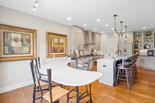 1107 Marcassin Dr, Columbia, MO 65201 - kitchen with high end range, wall chimney range hood, a kitchen bar, tasteful backsplash, and light wood finished floors