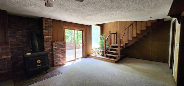 2716 Shagbark Cir, Jefferson City, MO 65109 - carpeted living area with wood walls, a wood stove, a textured ceiling, stairs, and ceiling fan